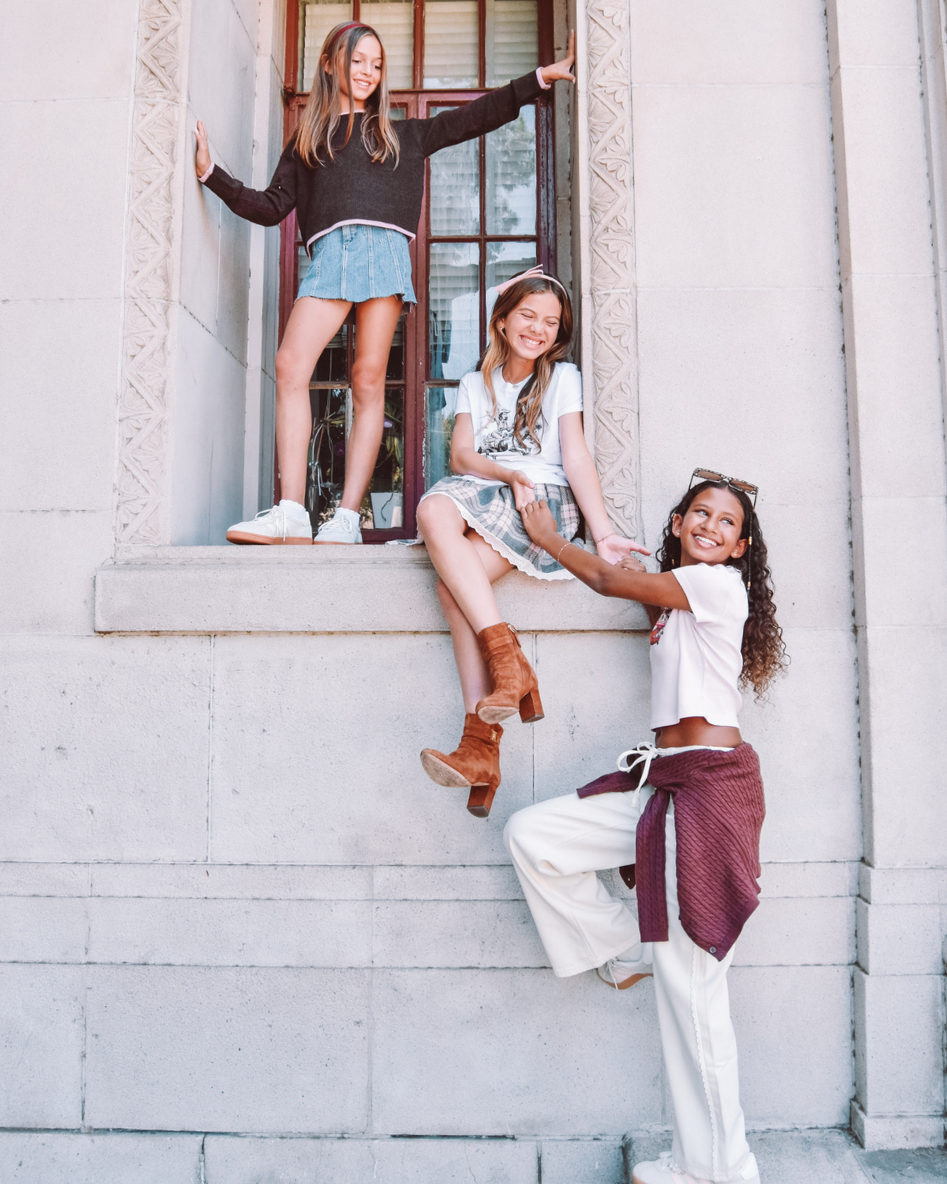 Three girls sneaking out of school! One girl stands in the window frame, another sits, and a third has just reached the ground.