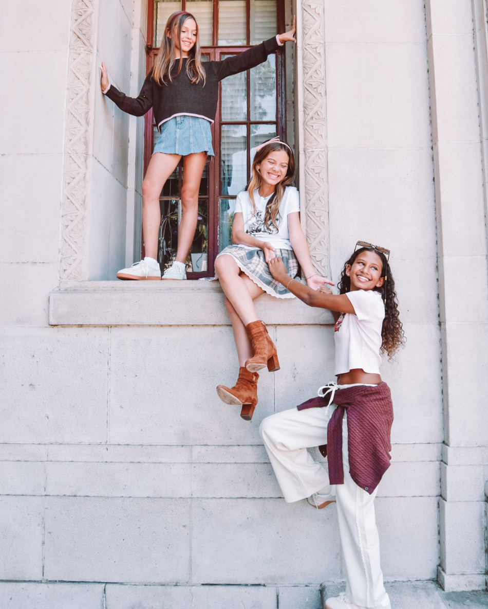 Three girls sneaking out of school! One girl stands in the window frame, another sits, and a third has just reached the ground.
