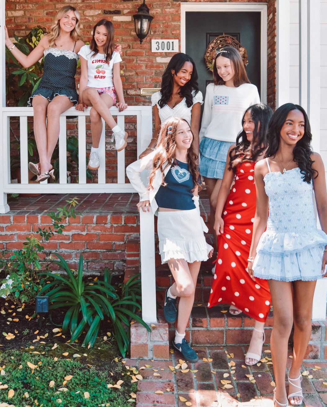 A group of 7 girls in red, white, and blue outfits on a porch getting ready for a summer BBQ.