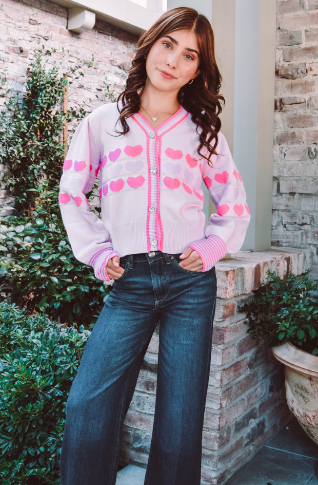 A girl with brown hair model a light pink heart cardigan with dark jeans.