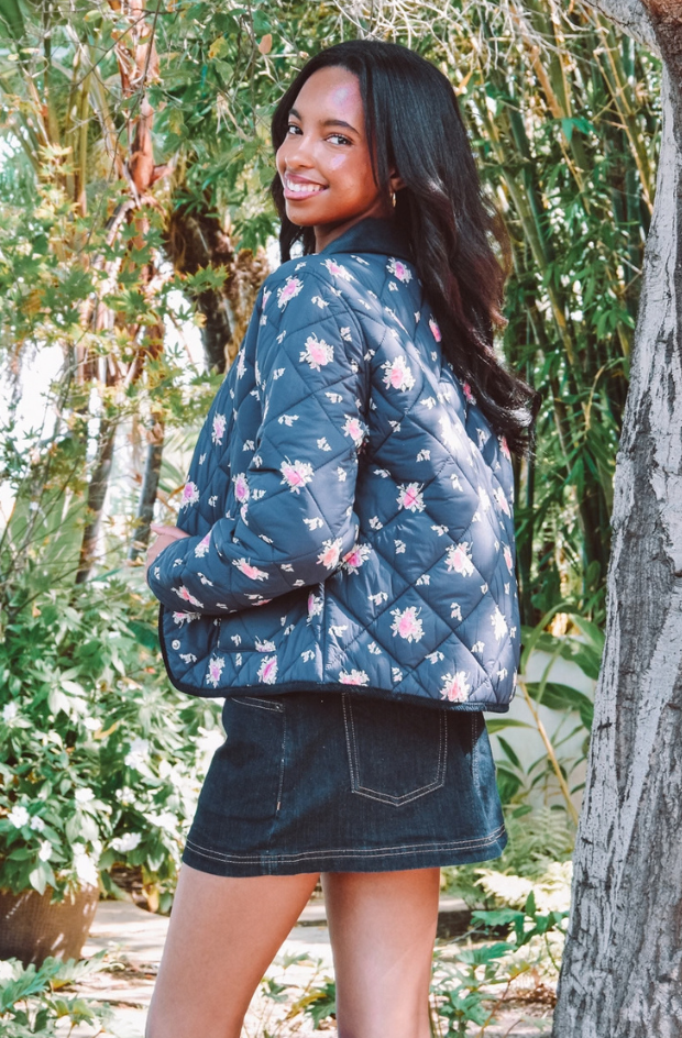 A teen girl looking over her shoulder smiling in a fall jacket and jean skirt
