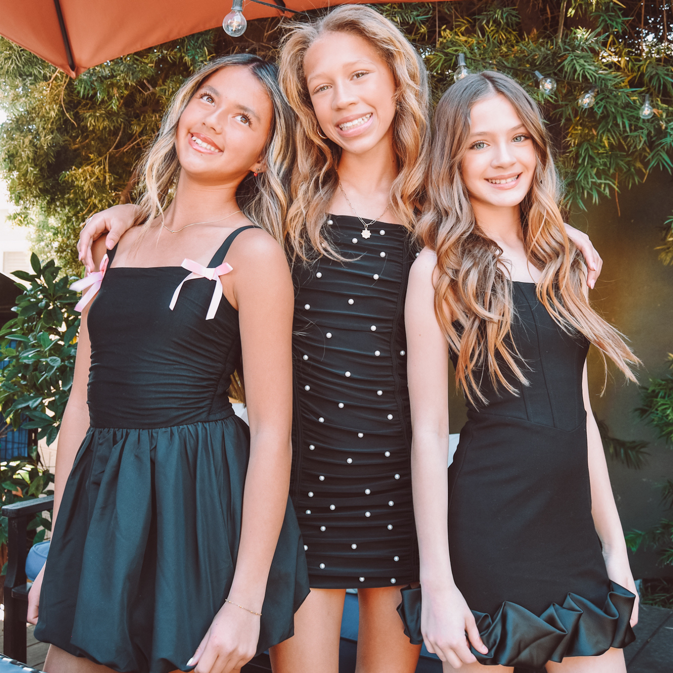 A group of three girls pose in little black dresses.