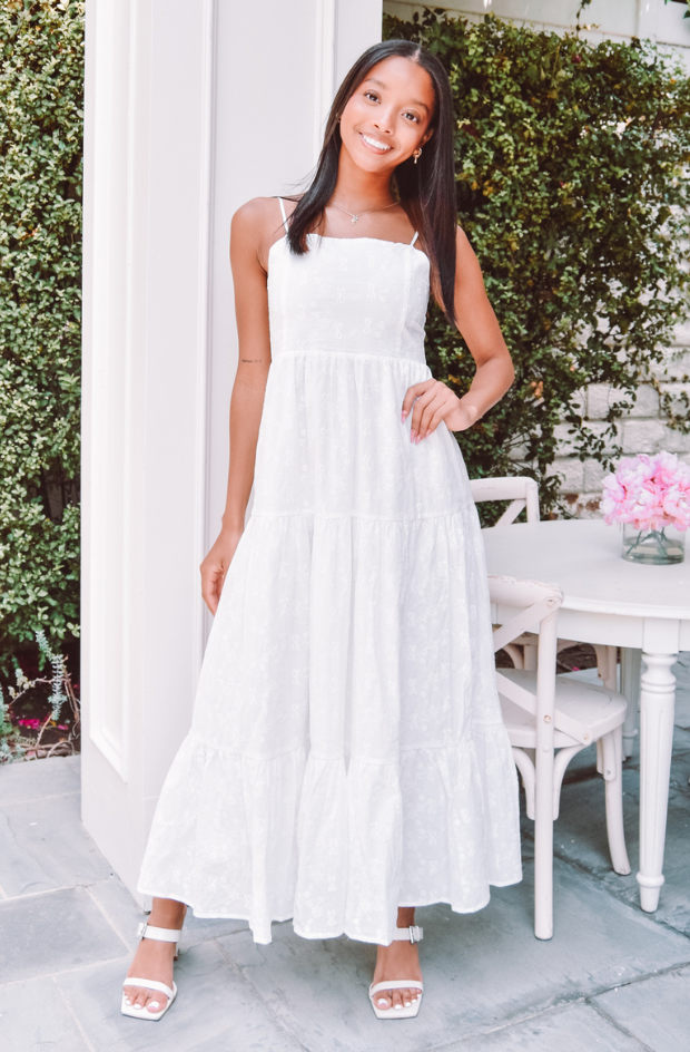 Young woman in a white maxi dress standing outdoors.