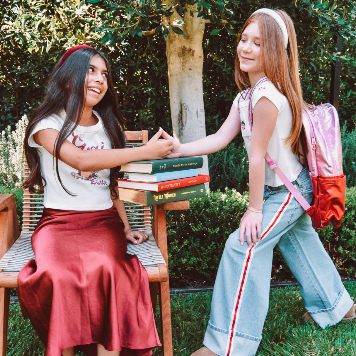 Two tween girls play thumb war on a stack of books wearing their First Day of School outfits.